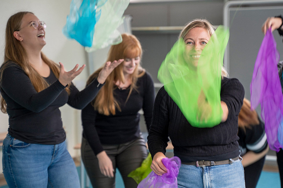 Teilnehmende einer pädagogischen Ausbildung werfen bunte Tücher
