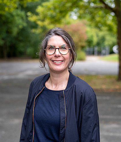 Lehrerin des Diakonie-Kollegs lächelnd vor Bäumen im Freien